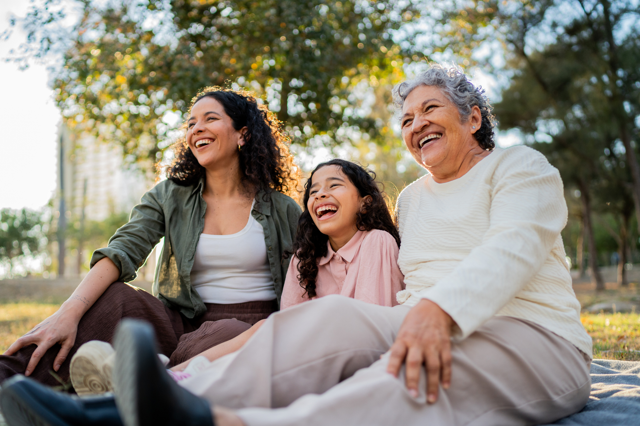 Grandmother, mother, and daughter laughing together in the park